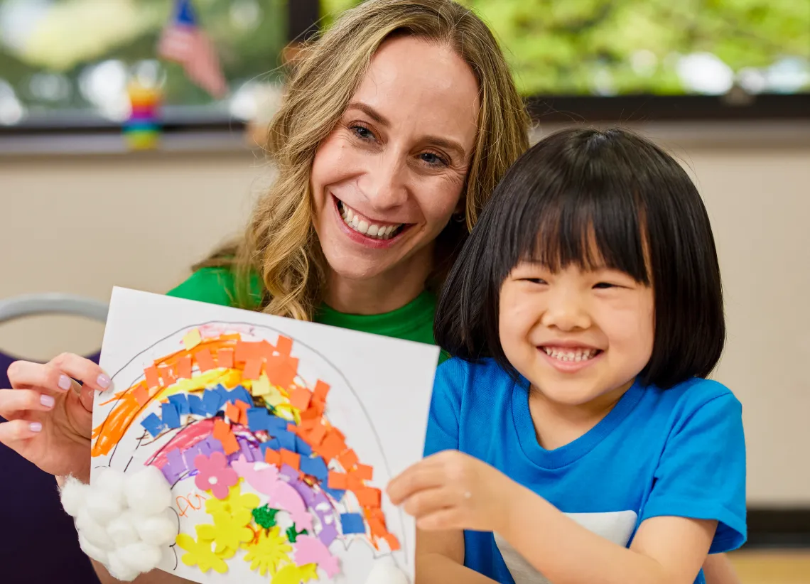 Kindergartner shows their artwork of a rainbow